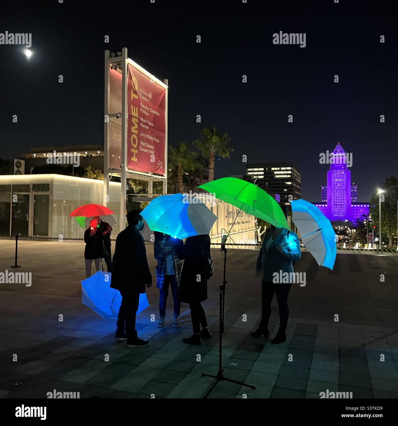 LOS ANGELES, CA, OCT 2021: Anonymous people with illuminated multi-color umbrellas at Music Center at night, with City Hall lit up purple in the background - Smartphone Captured Stock Image