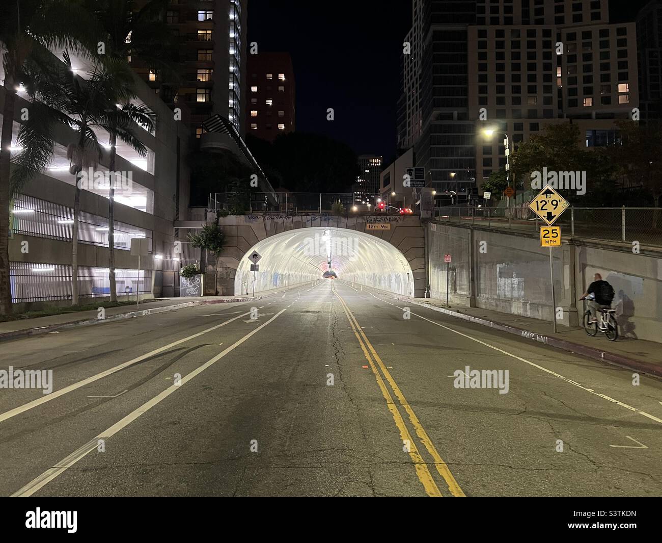 LOS ANGELES, CA, OCT 2021: Anonymous person rides a bicycle towards brightly lit Third Street Tunnel in Downtown at night - Smartphone Captured Stock Image