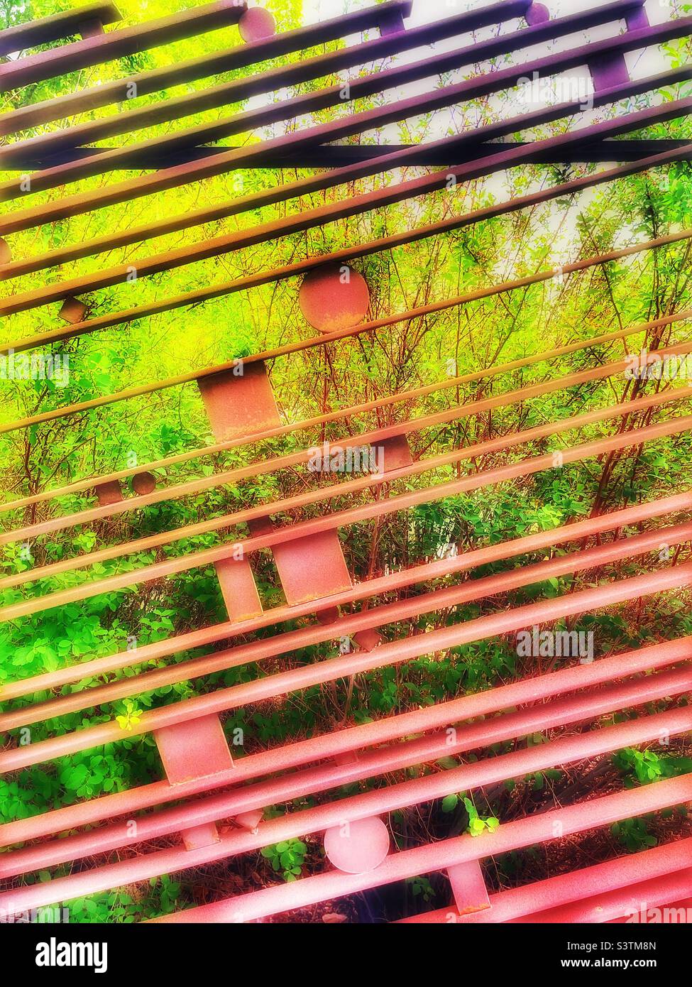 A rusty slanted iron fence encircles the outdoor courtyard of the Vernal  Dinosaur Museum. It’s design and ornate elements make an interesting pattern encircling this courtyard of statues and plants. - Smartphone Captured Stock Image