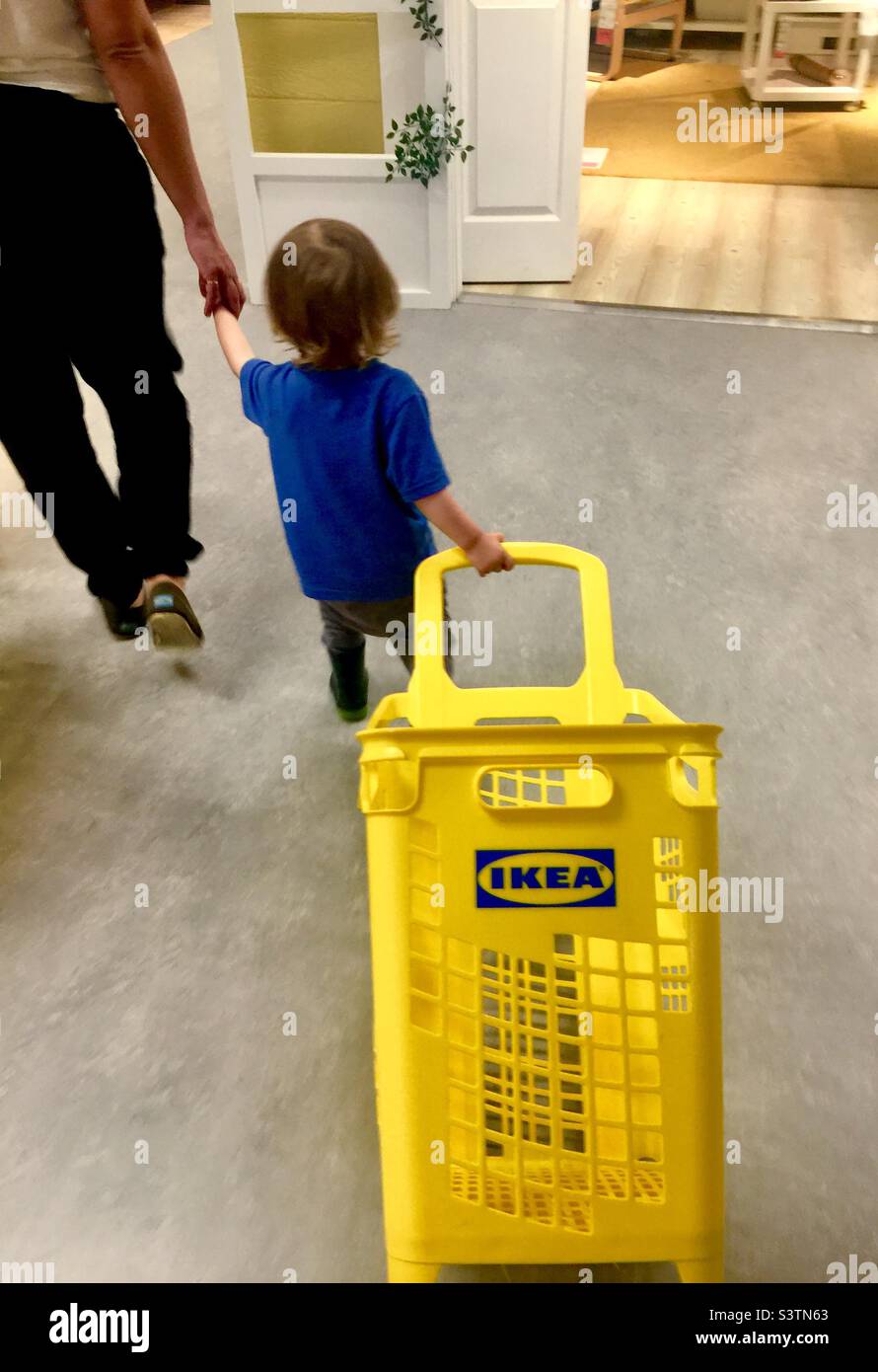 Family shopping at IKEA. Mother holds toddler’s hand who drags a shopping basket behind him. Canada. - Smartphone Captured Stock Image