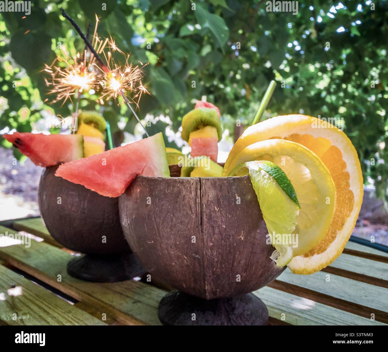 Fruity cocktails served in coconut shells and with sparklers under the shade of a tree Stock Photo