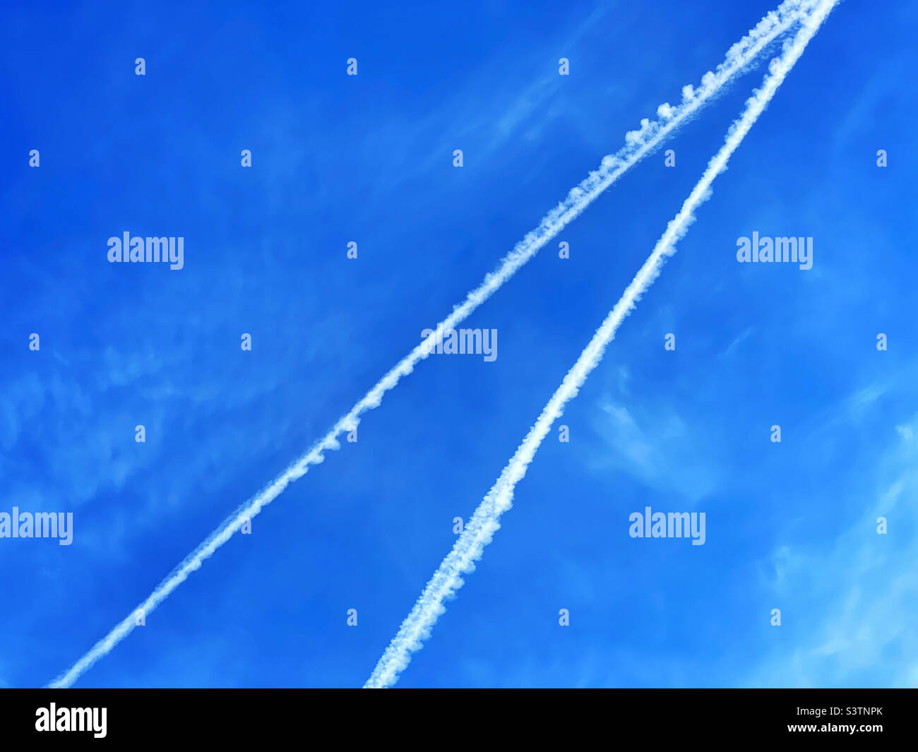 Two vapour trails in a blue sky. An abstract image of aviation. Did those aircraft collide? Have a near miss? Cross over with plenty of time to spare? Photo ©️ COLIN HOSKINS. Stock Photo