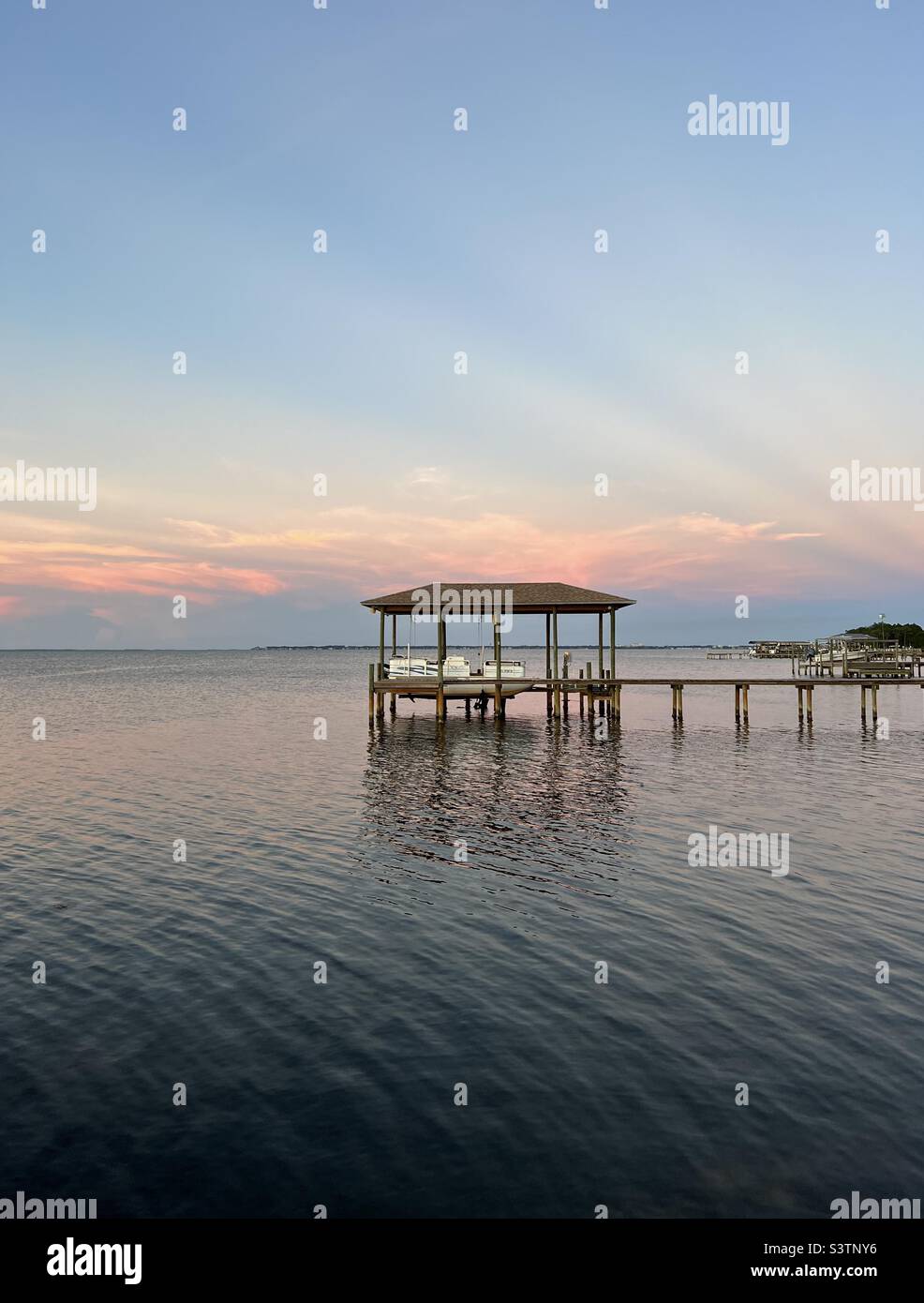 Sunset over bay water with antisolar rays and boat dock Stock Photo