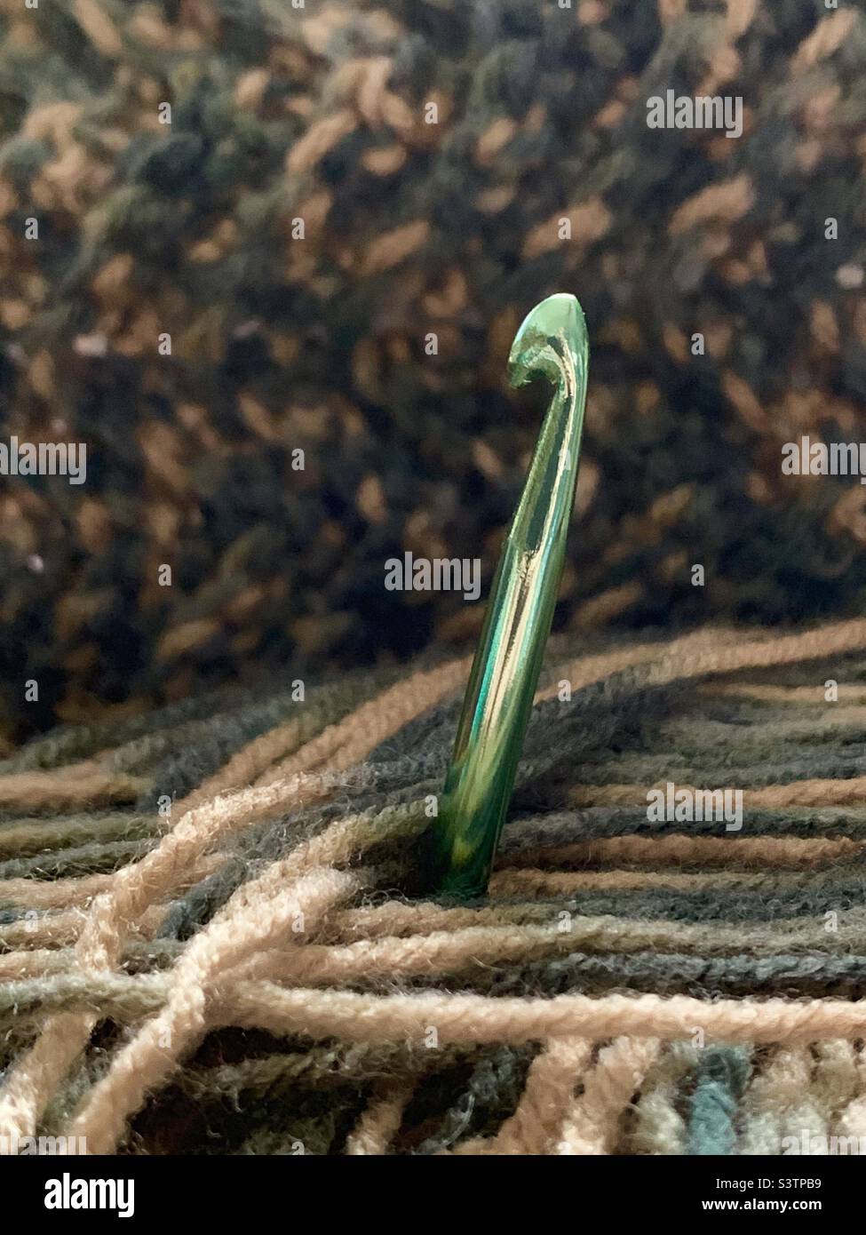 Green aluminum crochet hook in ball of yarn with crocheted blanket in background Stock Photo