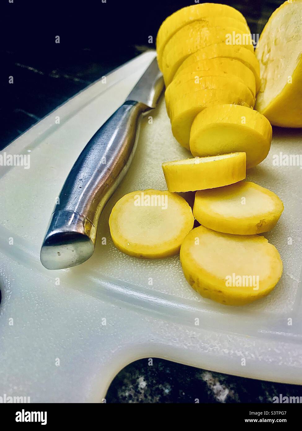 Yellow squash, sliced on white cutting board with knife Stock Photo