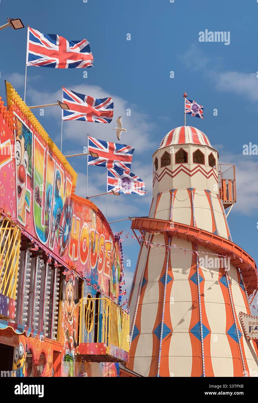 British Seaside funfair- UK Union Flags flying at a seaside fun ride amusement park in Hunstanton Norfolk coast - summer Britain jubilee flags summertime seagull Stock Photo