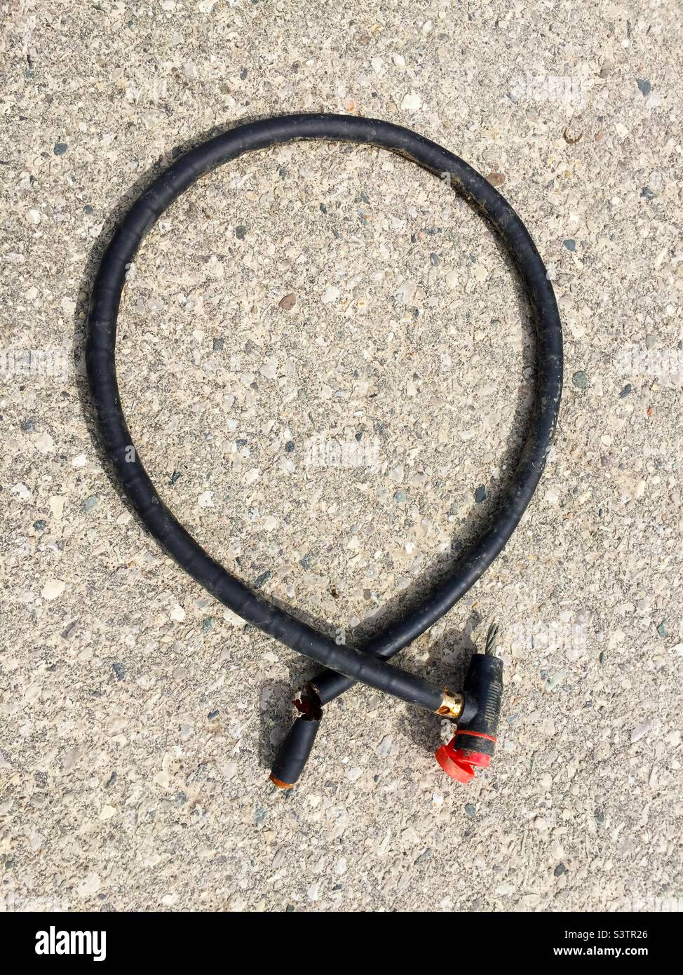 Cut lock cable, after a bike is stolen, Ontario, Canada. Left behind on the pavement. Not very secure lock. Stock Photo