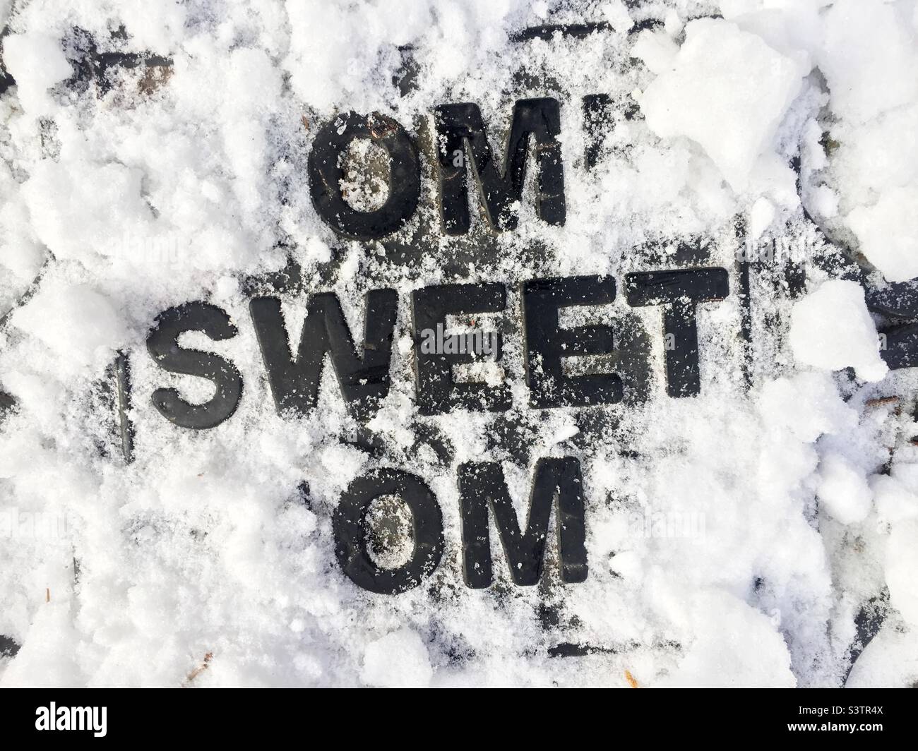 Home Sweet Home doormat, partially covered in snow, becomes a New Age chant — Om, Sweet, Om — Ontario, Canada. Stock Photo