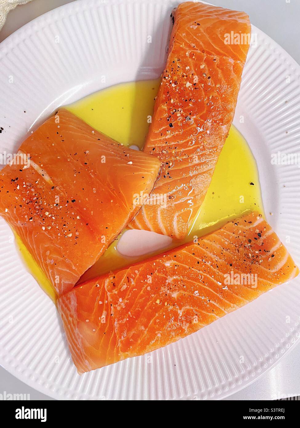 Three fresh salmon fillets prepped ready to cook with spices and olive oil in a residential kitchen, 2022, USA - Smartphone Captured Stock Image