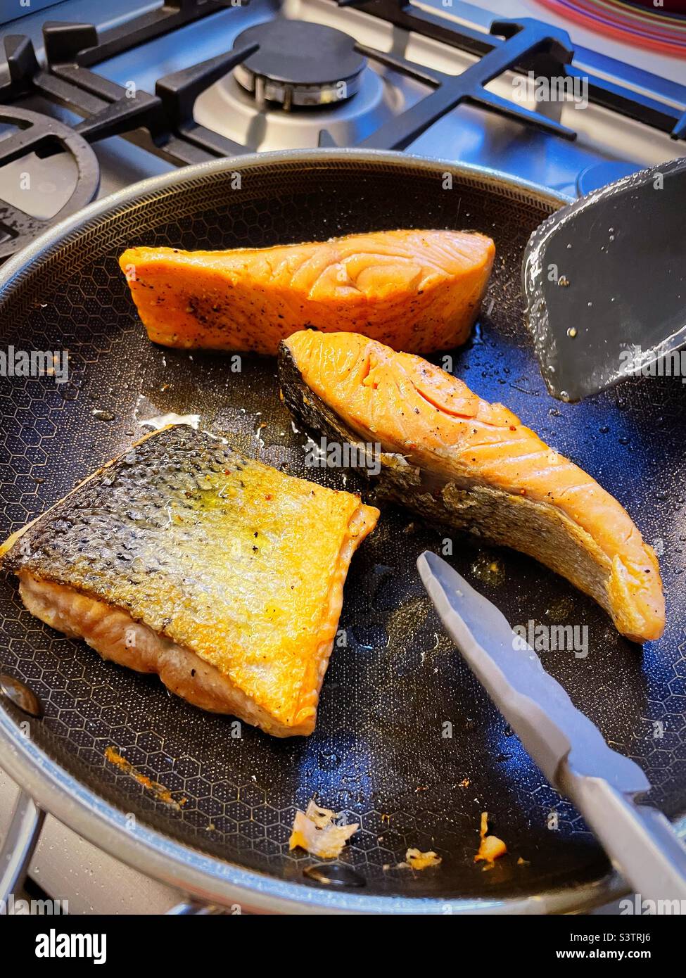 Fresh salmon fillets being seared in a skillet on a residential stove top, 2022, USA Stock Photo