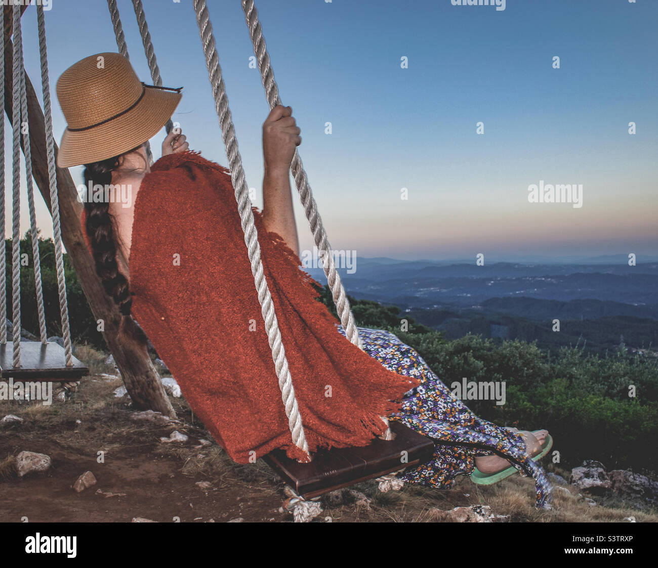 Woman in summer hat and a light wrap, swings and enjoys the early evening view of the landscape - Smartphone Captured Stock Image