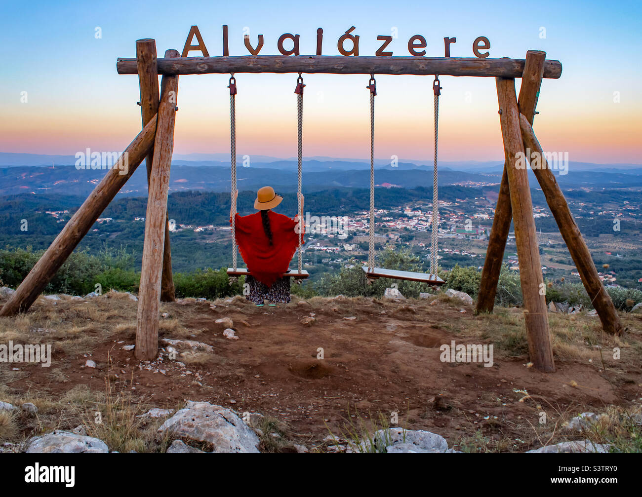 A women in a summer hat and light wrap, enjoys the summer evening view across Alvaiazere from a swing high above the town - Smartphone Captured Stock Image