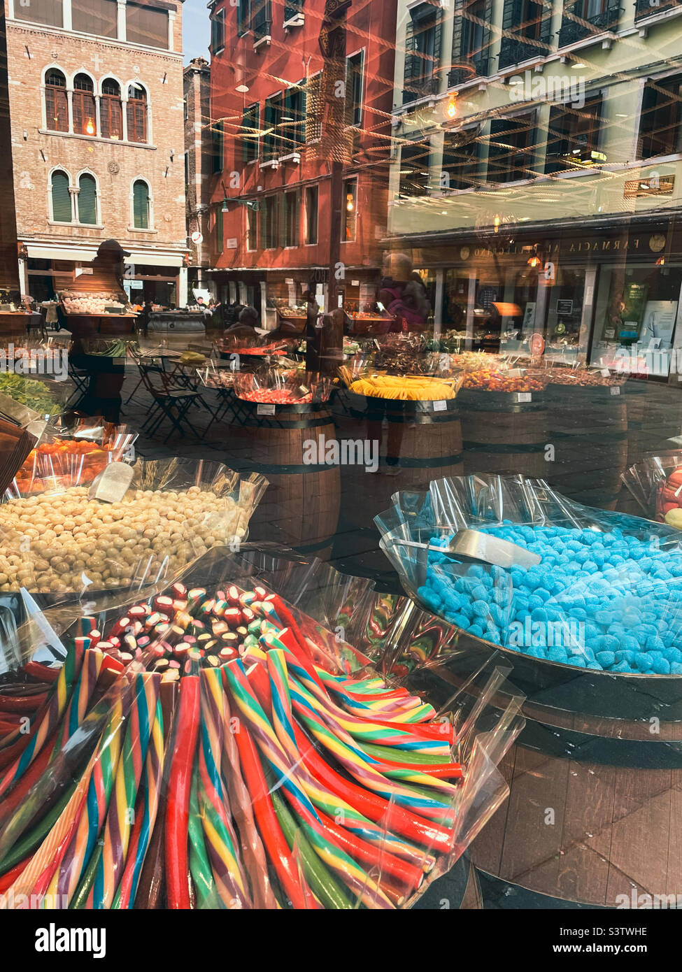 Candy shop with colourful candy displayed in wooden barrels in Venice with buildings and people reflecting in the glass. - Smartphone Captured Stock Image