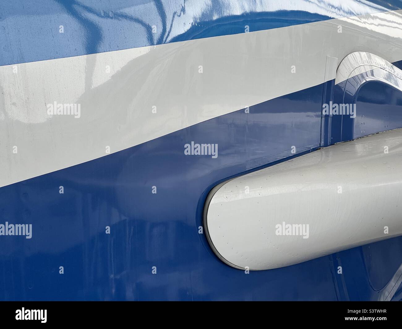 Close up view of fuselage of passenger aircraft exterior, light blue and dark blue stripes on white with reflections. Suitable for background for graphics and text - Smartphone Captured Stock Image