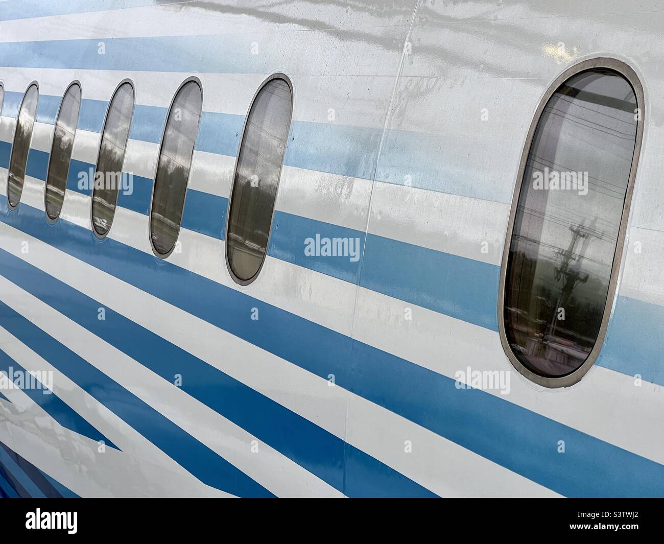 Detail of fuselage of passenger aircraft exterior, with blue and white stripes around passenger windows. Suitable for background for graphics and text - Smartphone Captured Stock Image