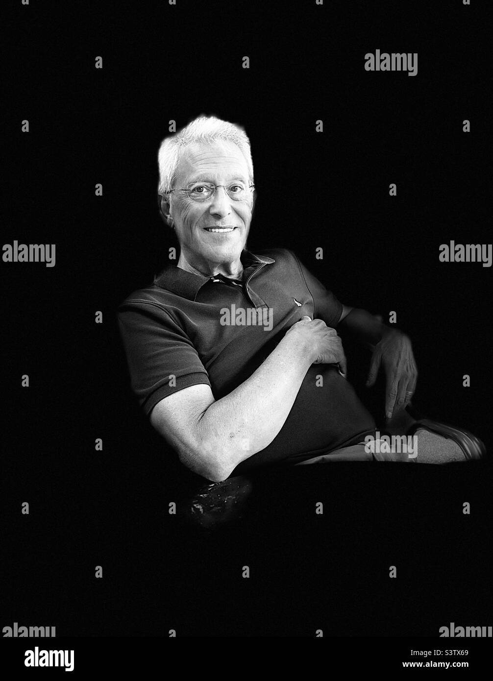 Happy senior male posing in a chair against a black background. Stock Photo