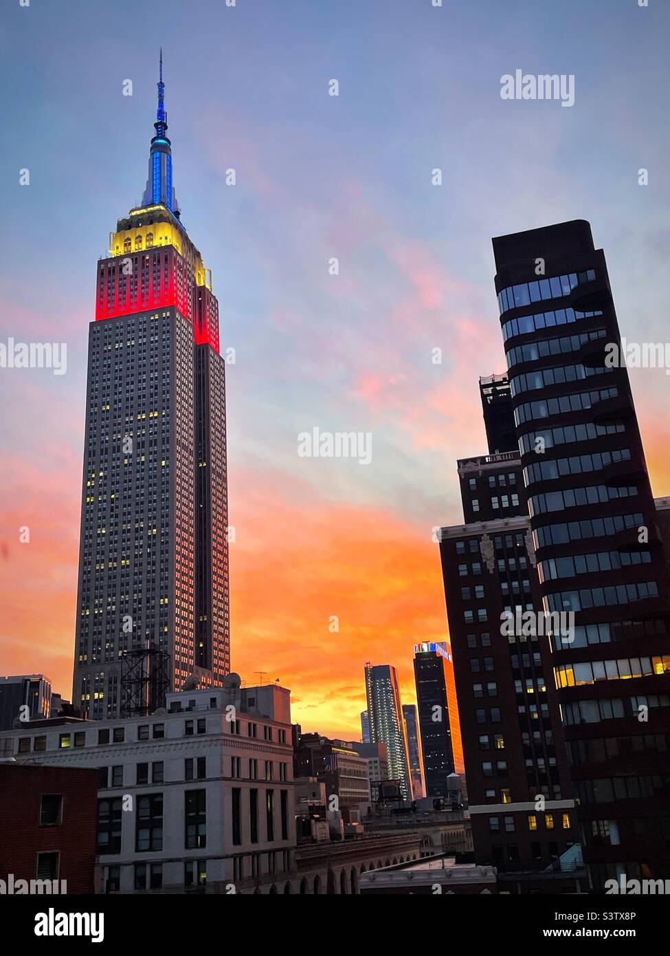 Sunset with a red white and blue brightly lighted Empire State building in the foreground, 2022, New York City, USA Stock Photo