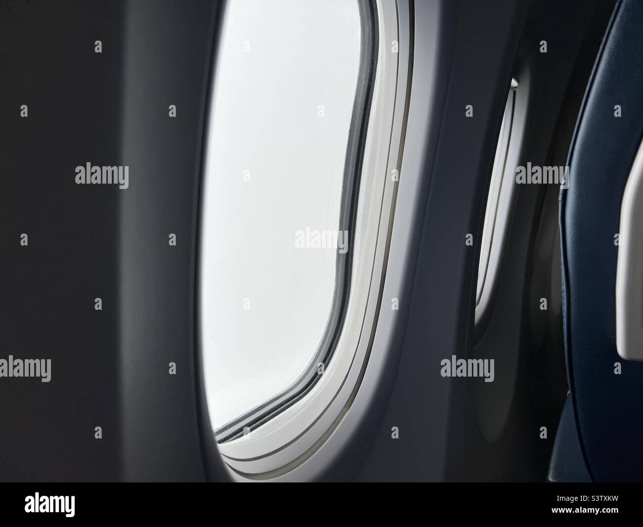 Angled view through silhouetted airplane windows filled with white as aircraft flies through clouds - Smartphone Captured Stock Image