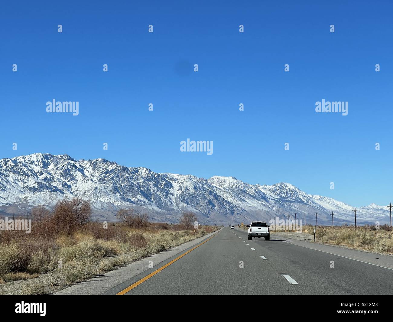 View of road with white pickup truck ahead, driving towards mountains