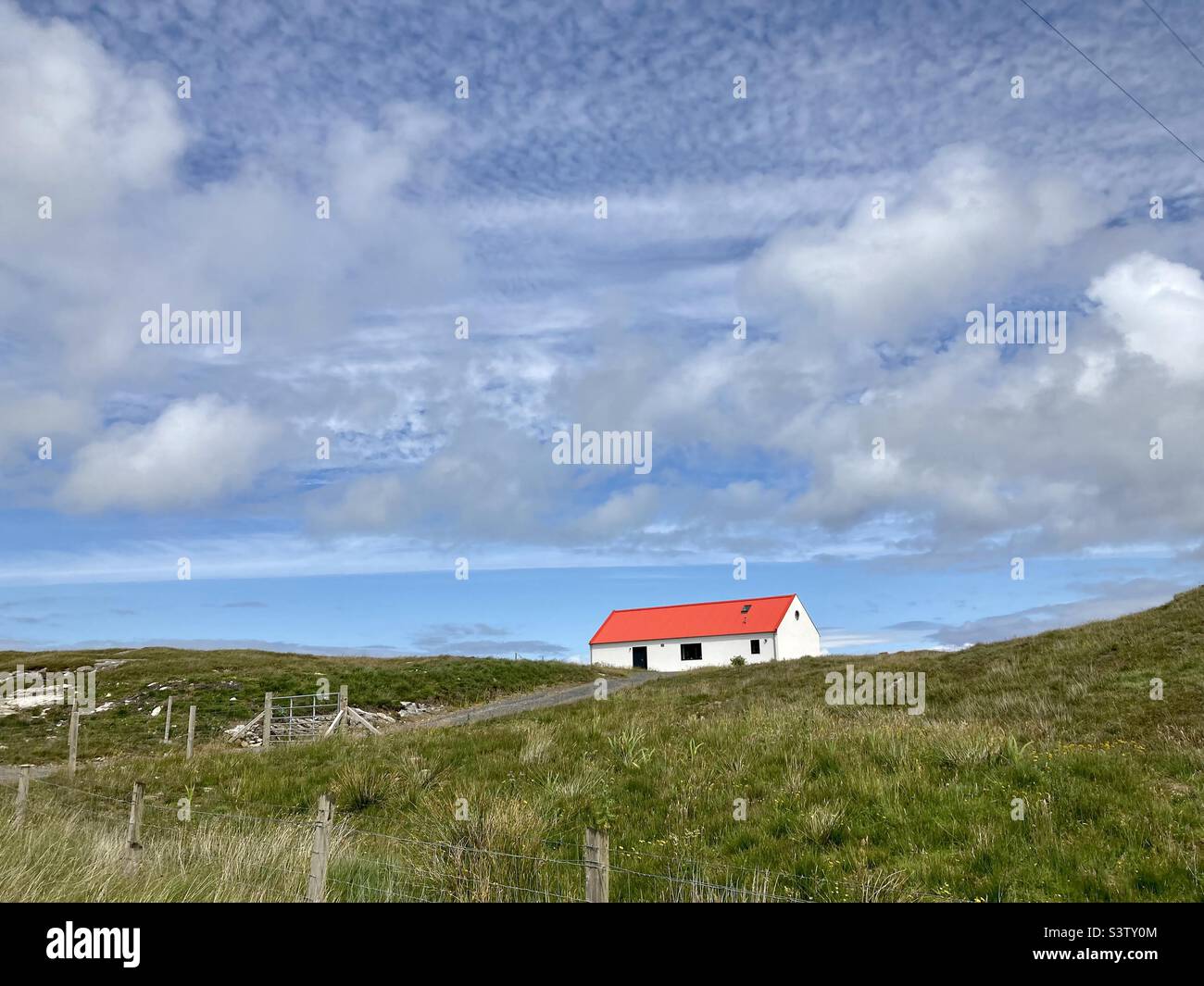 A white house with bright red roof standing alone and isolated, Isle of Barra, Outer Hebrides, Scotland - Smartphone Captured Stock Image