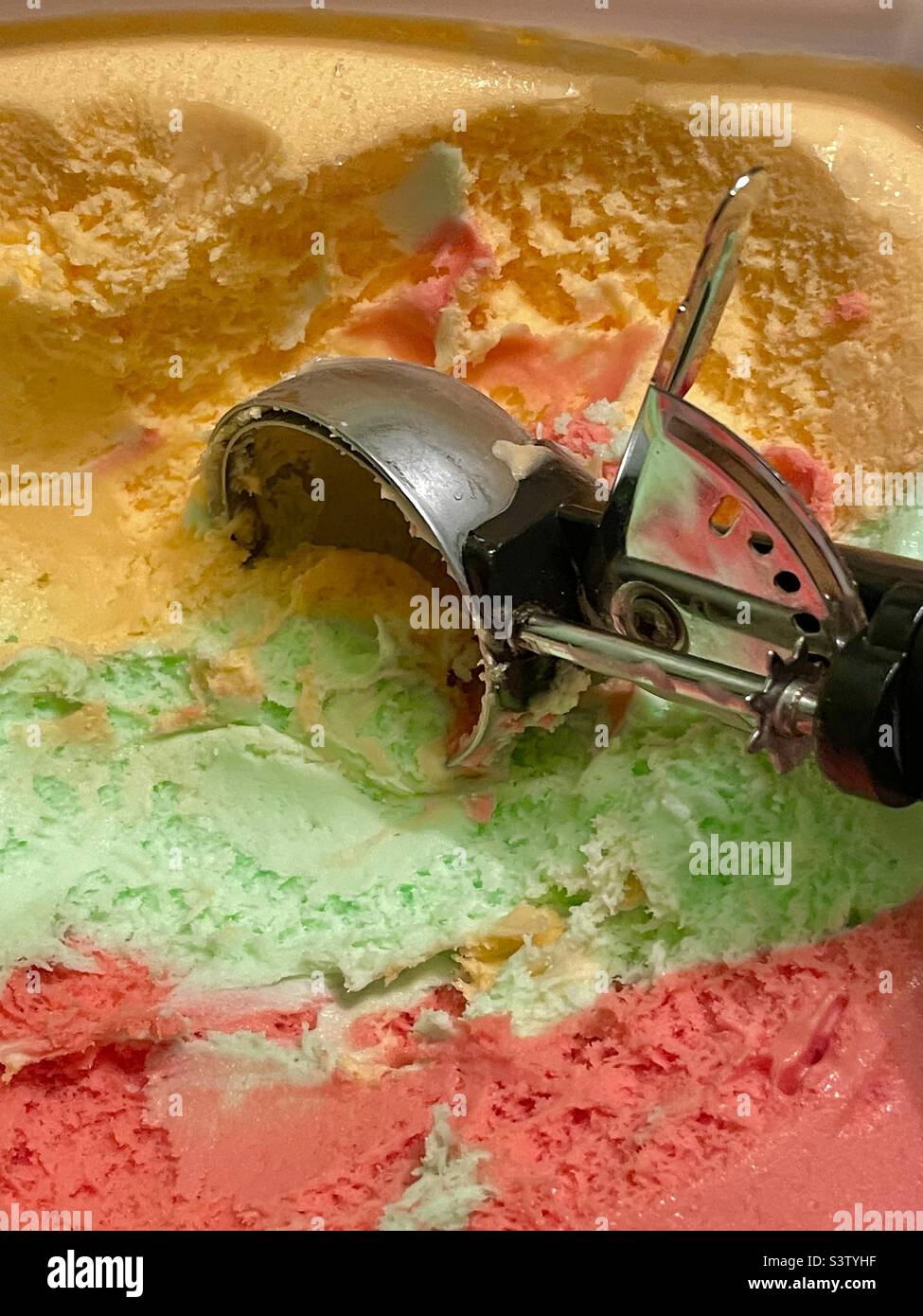 An ice cream scoop in a gallon of Rainbow Sherbet ice cream ready to start filling up all the bowls and cones of ice cream lovers. - Smartphone Captured Stock Image