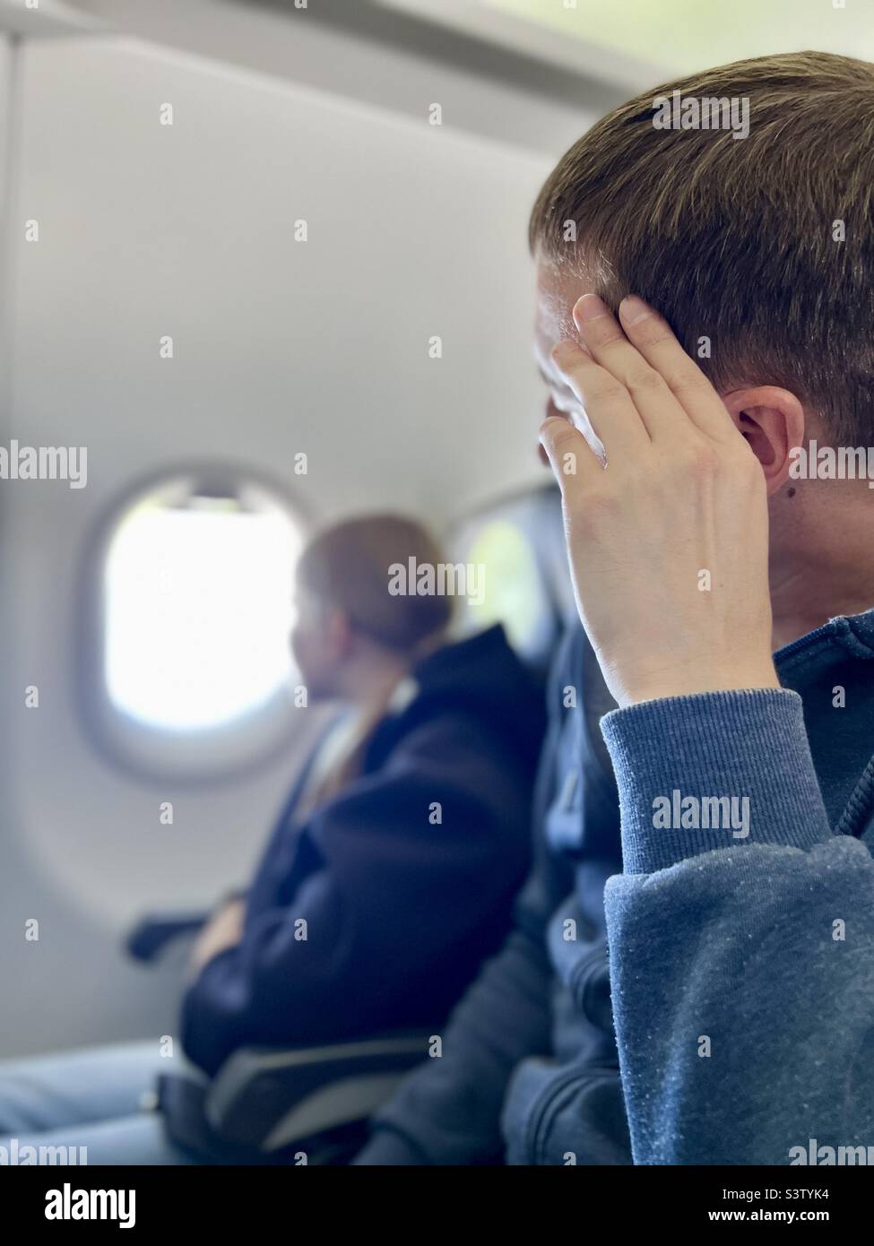 father and daughter are sitting on the plane.  people travel by air.  teenager looks out the window of the plane. Stock Photo