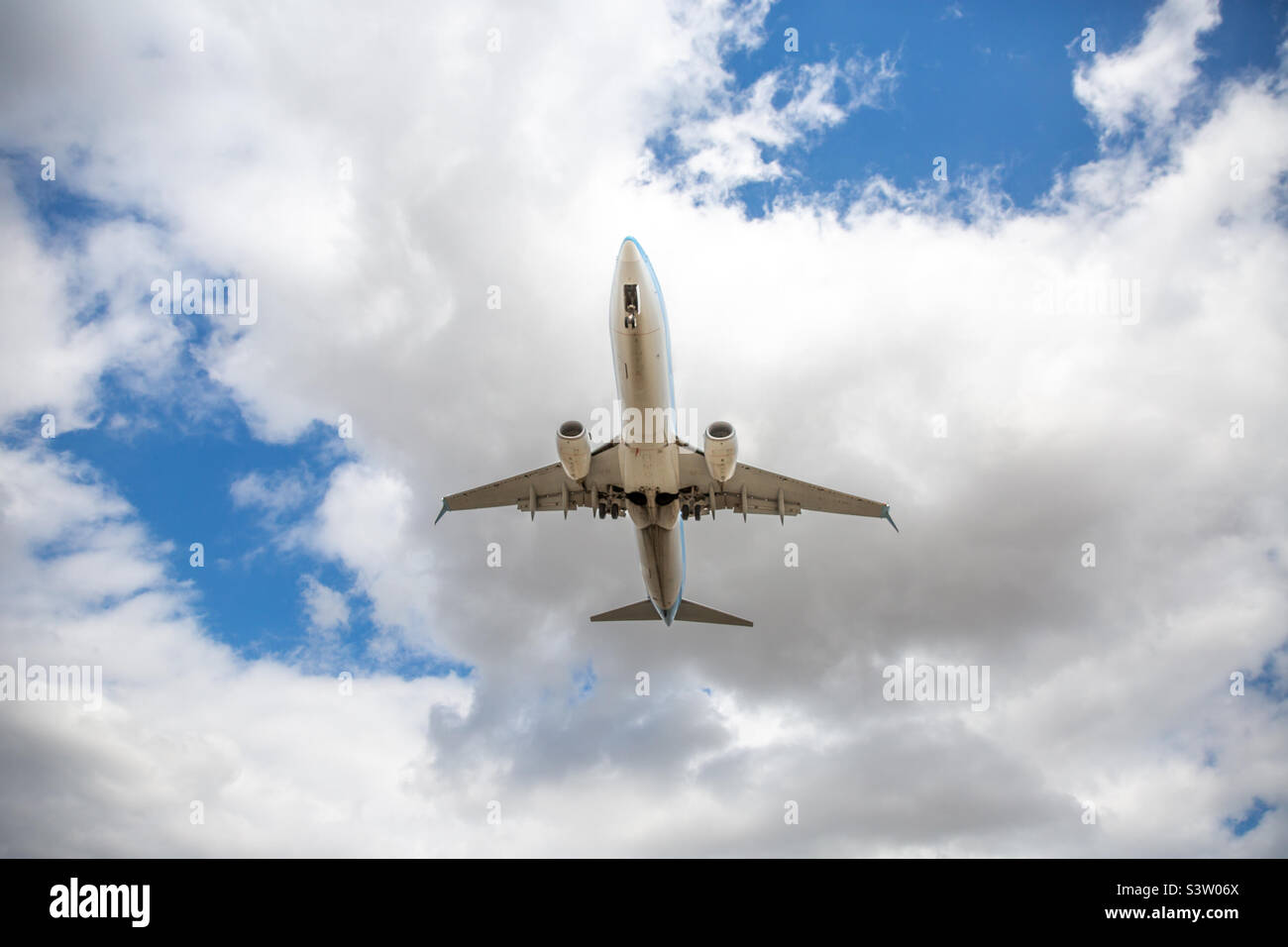 Directly underneath a low flying passenger plane taking off or landing with clouds behind and copy space Stock Photo