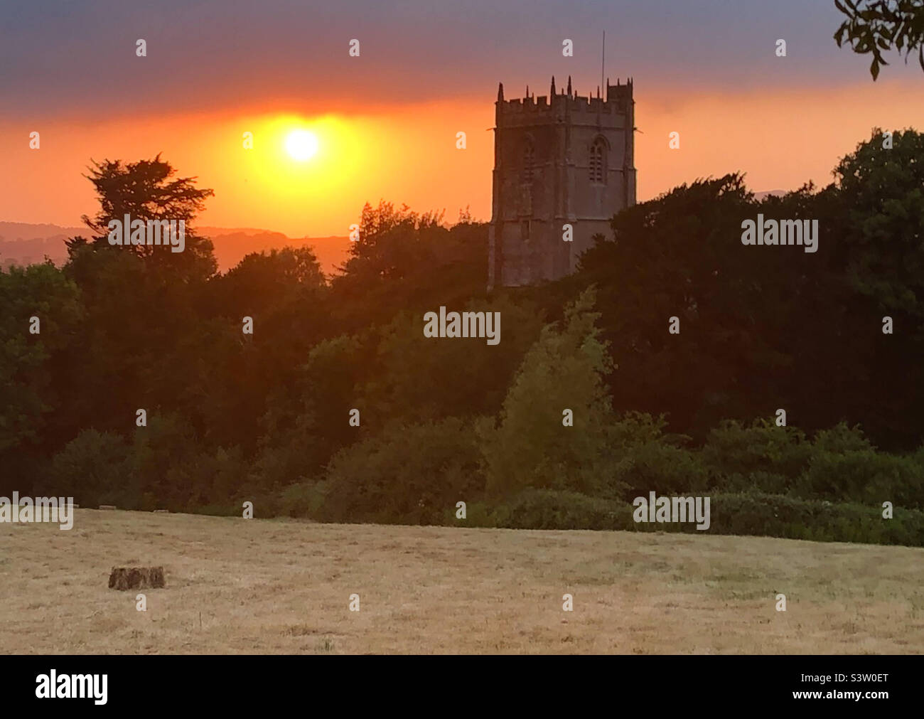 Whitchurch Canonicorum, Dorset, England, United Kingdom, 19th July 2022. Summer sunset over St Candida and Holy Cross church tower on the hottest day of the year - Smartphone Captured Stock Image