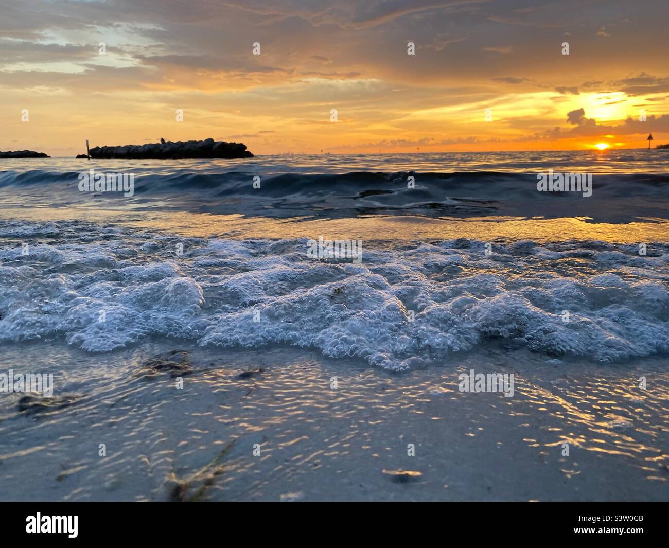 Small wave crashing on beach at sunset Stock Photo