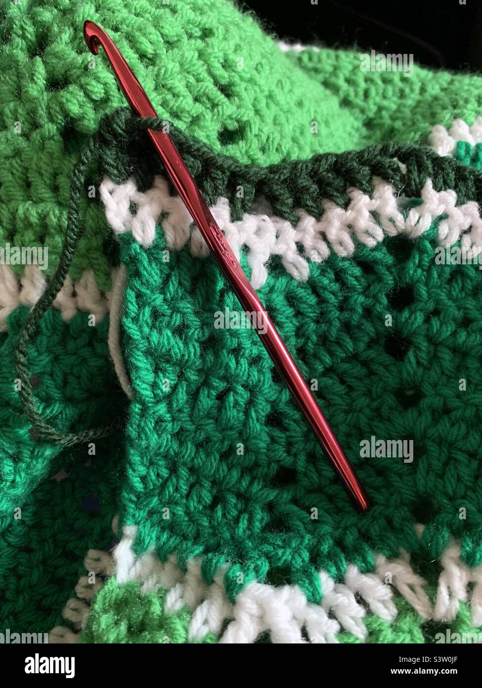 Red aluminum crochet hook with green and white crocheted chevron pattern blanket Stock Photo