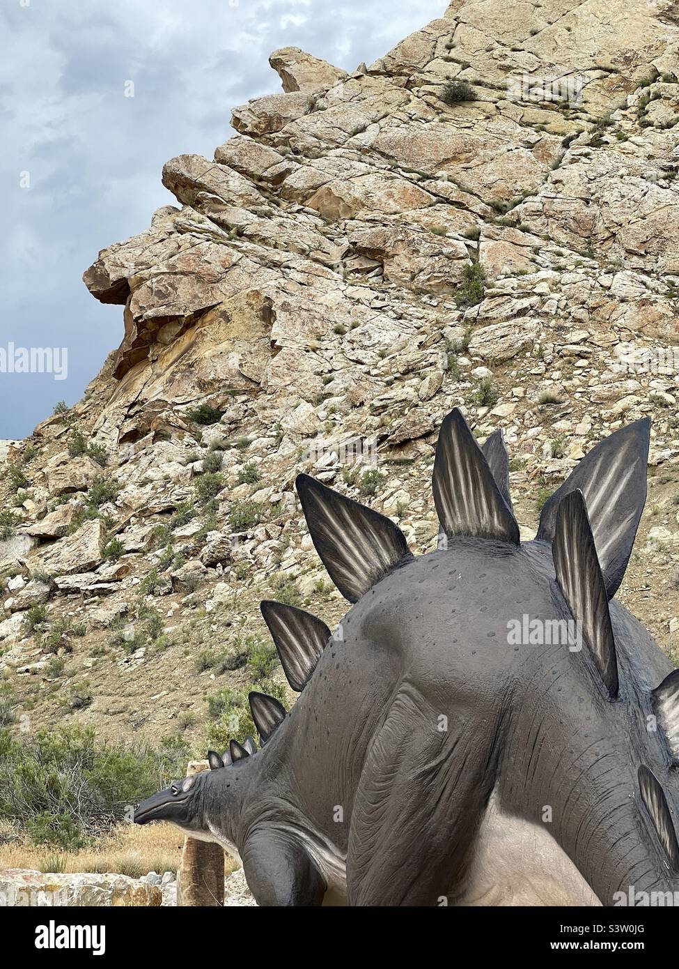 Upon entering the Visitor Center at the Dinosaur National Monument in Vernal, Ut., USA this dinosaur statue greets visitors. Funnily, the fins along its’ back look much like the jagged rocks behind it - Smartphone Captured Stock Image