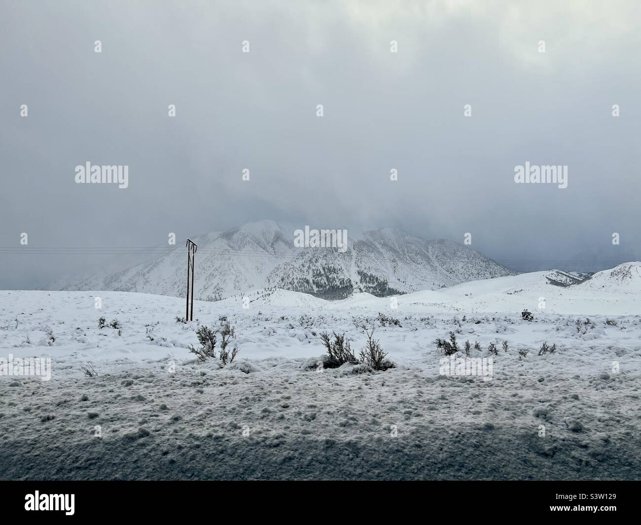 Low clouds over mountain tops with snow covered landscape in foreground, on a cold, winter's day, near Mammoth Lakes ski and snowboarding resort, California - Smartphone Captured Stock Image