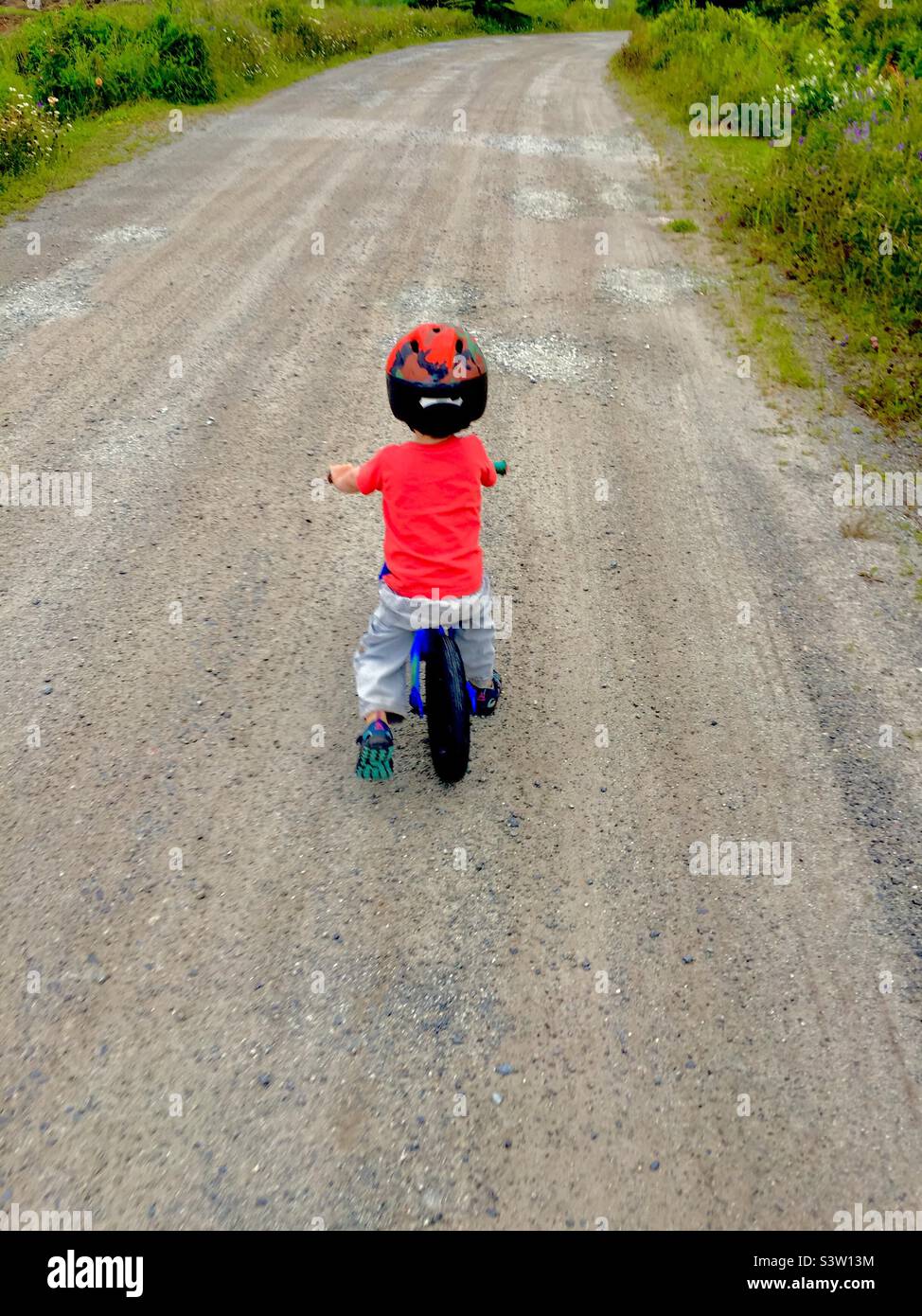 Toddler on a Balance Bike on a long, rough road, Halifax, Canada. Outdoors. As far as the eye can see. Where to? Stock Photo
