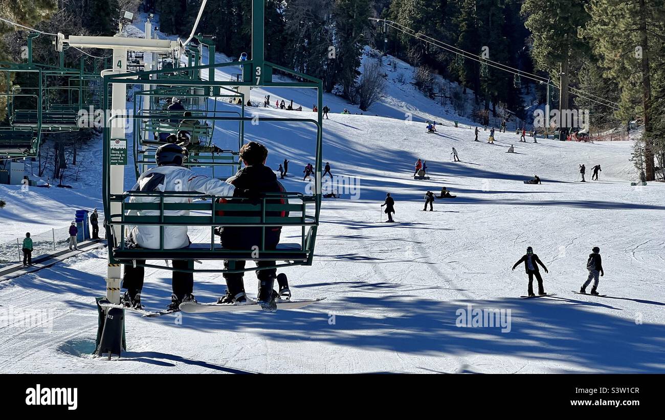Anonymous riders on chair lift at Snow Summit in California, with other skiers and snowboarders on snow-covered slopes beneath them - Smartphone Captured Stock Image