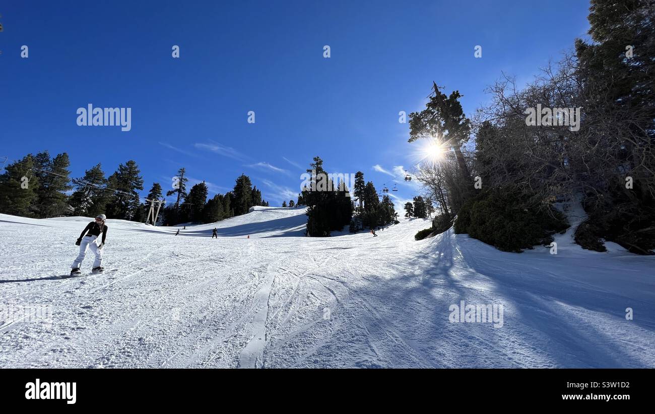 BIG BEAR, CA, JAN 2022: Anonymous snowboarder passing with other snowboarders and skiers at Big Bear Mountain, California. Low sun coming through trees behind - Smartphone Captured Stock Image