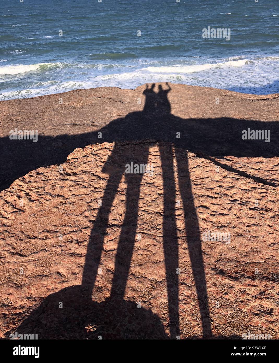 Long shadows of people on the cliffs by the sea. - Smartphone Captured Stock Image