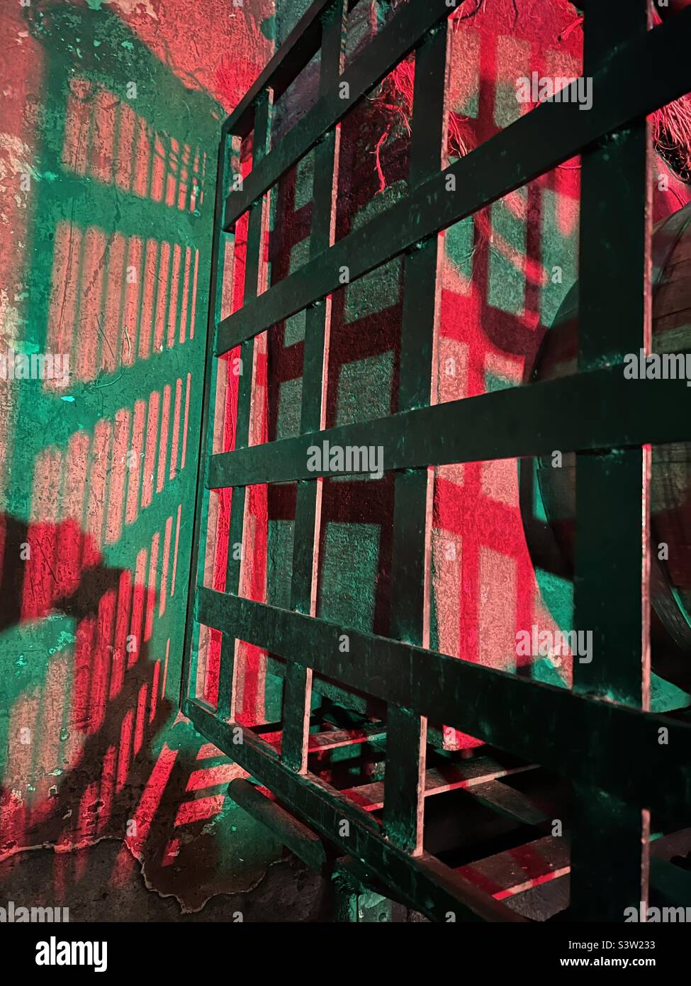 Abstract pattern of green shadows on concrete and red light through metal grating, creating grungy background image - Smartphone Captured Stock Image