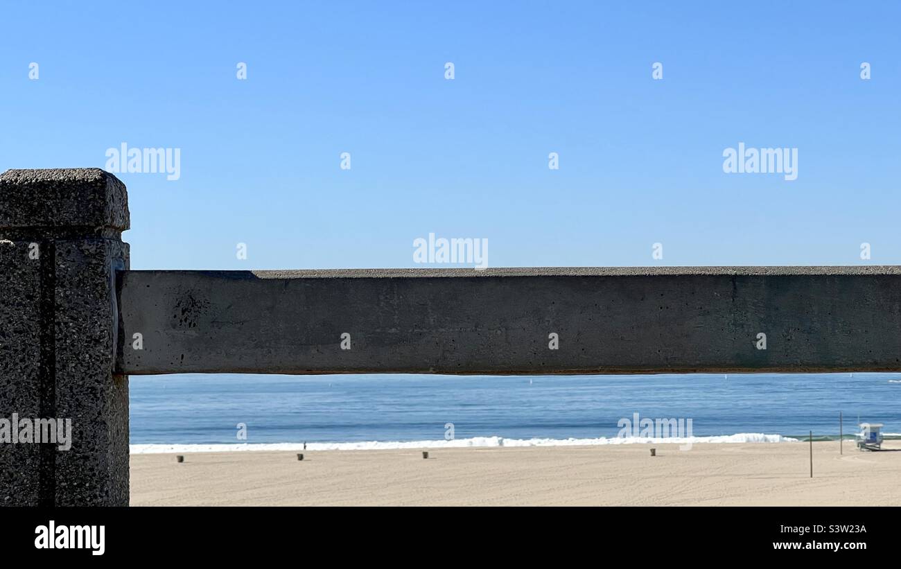 Focus on concrete fence post and railing in foreground, with soft focus beach, sea and life guard hut behind in southern California - Smartphone Captured Stock Image