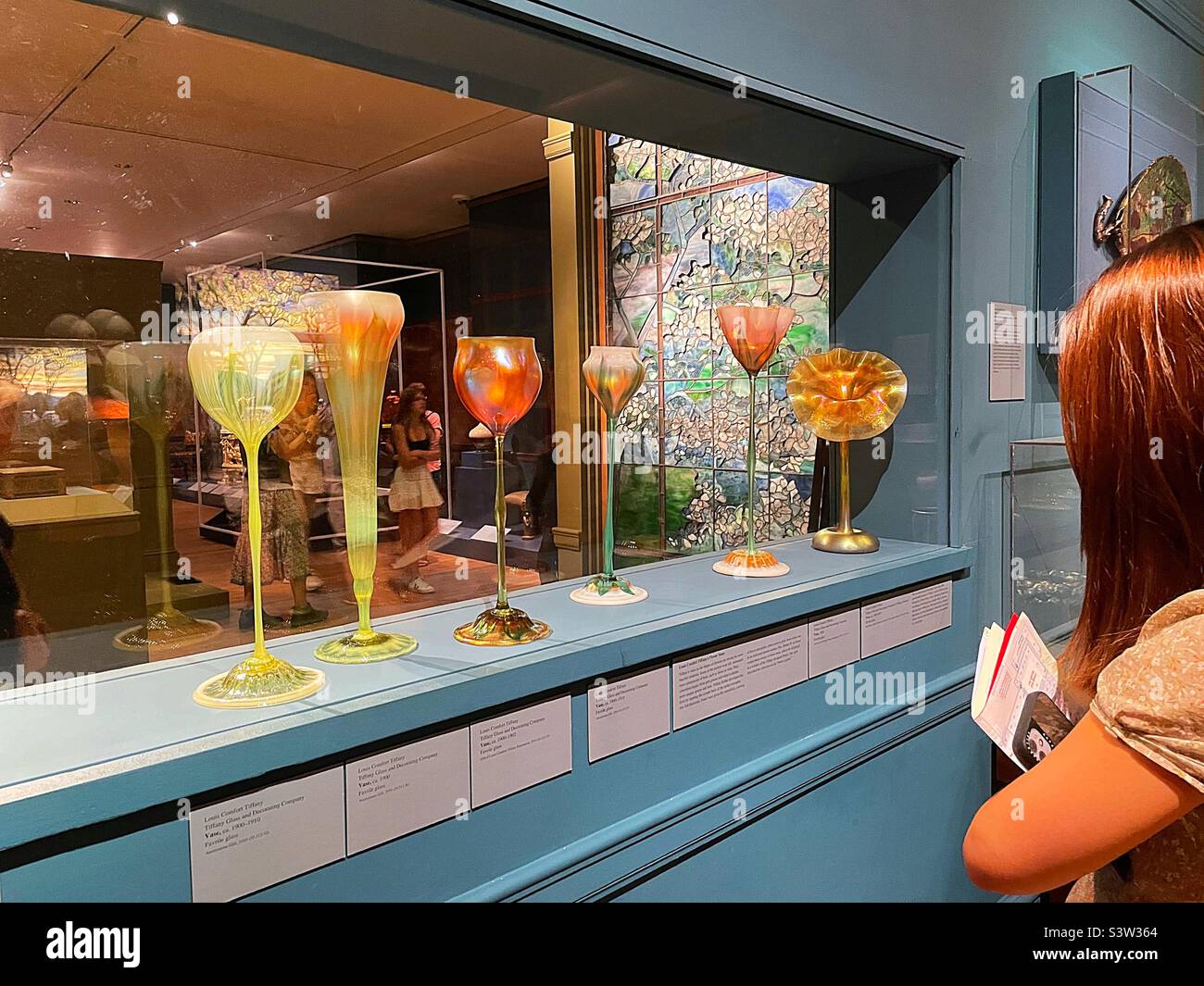 Visitors admire the hand blown glass art pieces in the Tiffany Area of the American wing, metropolitan museum of art, 2022, New York City, United States Stock Photo