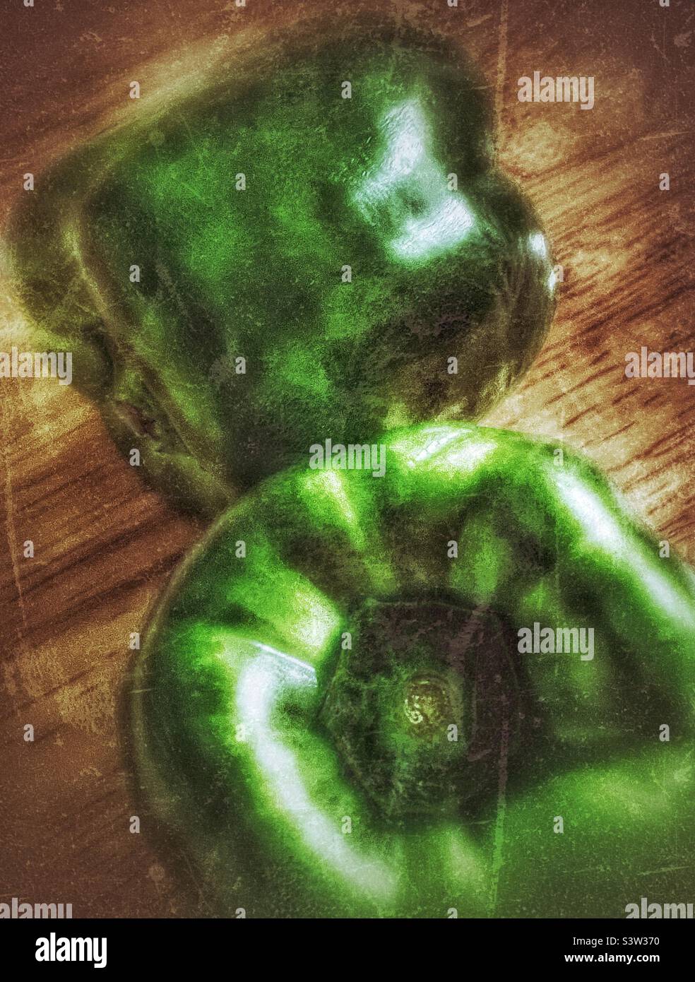 Still life image of a pair of green peppers on a wood block table with dramatic lighting. Grunge effect digitally added for artistic effect. - Smartphone Captured Stock Image