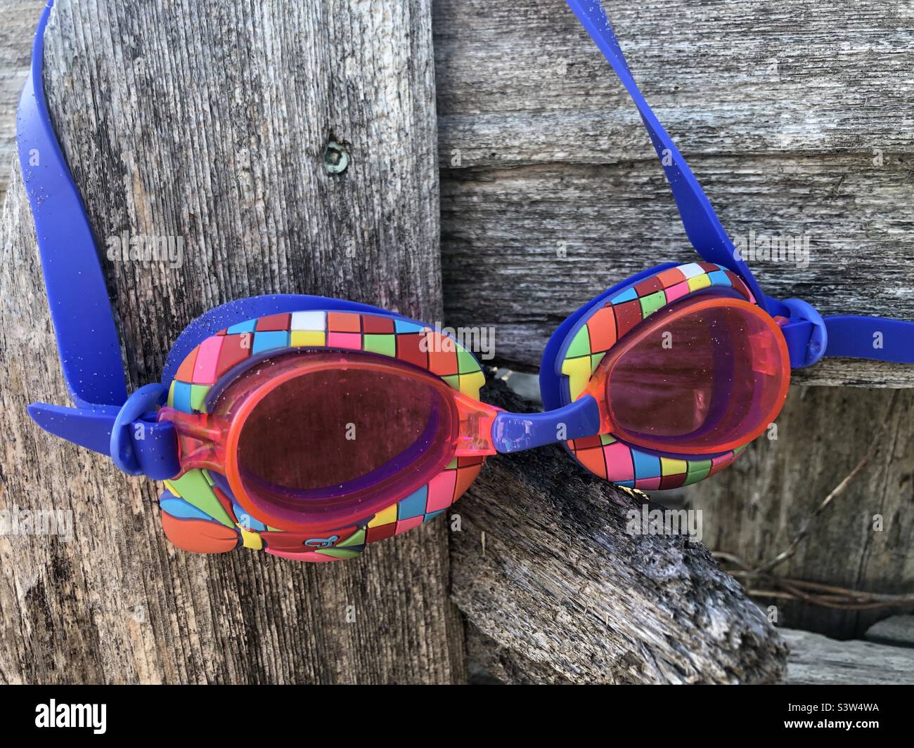 Colourful swimming goggles hanging on a wooden fence. Stock Photo