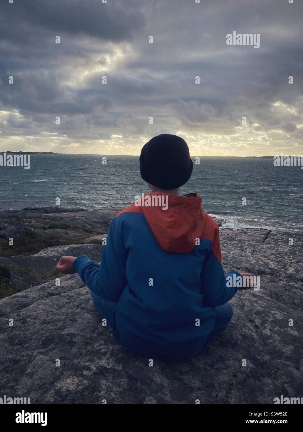 A boy at the age of eleven or twelve Watching the baltic sea on the Swedish West Coast during a storm in a yoga pose Stock Photo