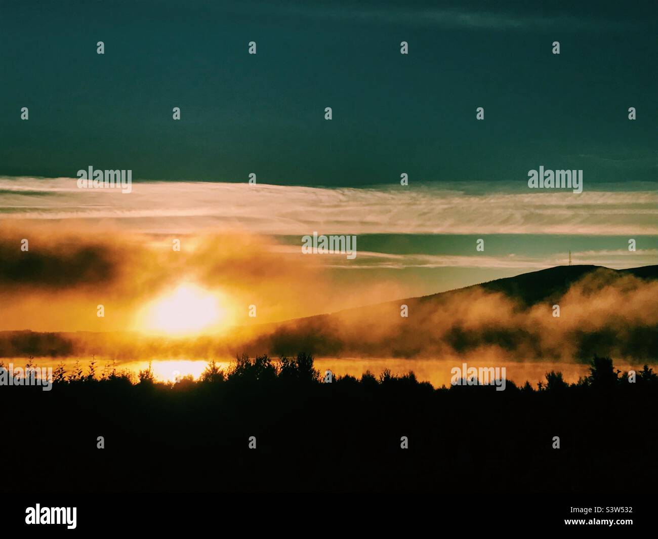 Mist rising over clatteringshaws loch at sunrise in Galloway forest park, Scotland - Smartphone Captured Stock Image
