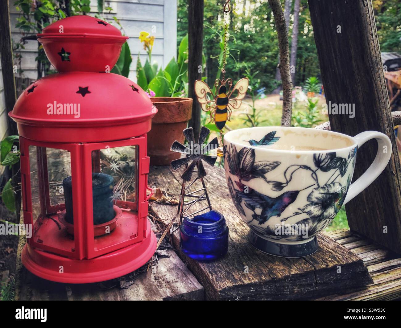 Coffee al fresco- outdoor still life with coffee cup, windmill curio, candle lamp, and clay pot Stock Photo