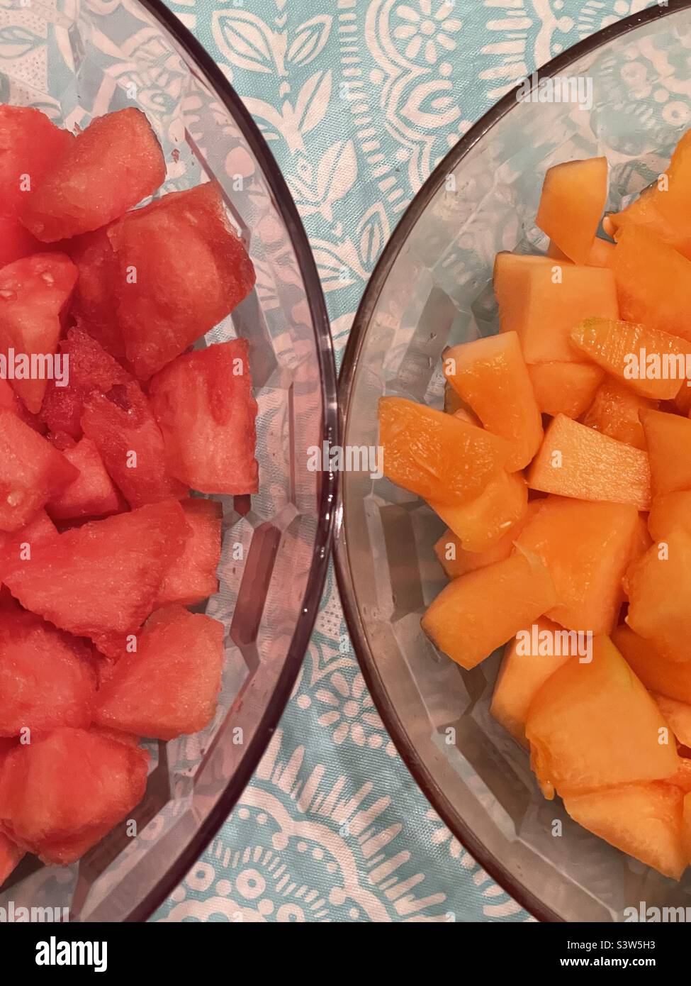 Two large bowls, side by side, sit on a tabletop filled with fresh cut fruit. One bowl holds delicious cantaloupe and the other juicy watermelon. Natural organic colors of orange and red. - Smartphone Captured Stock Image