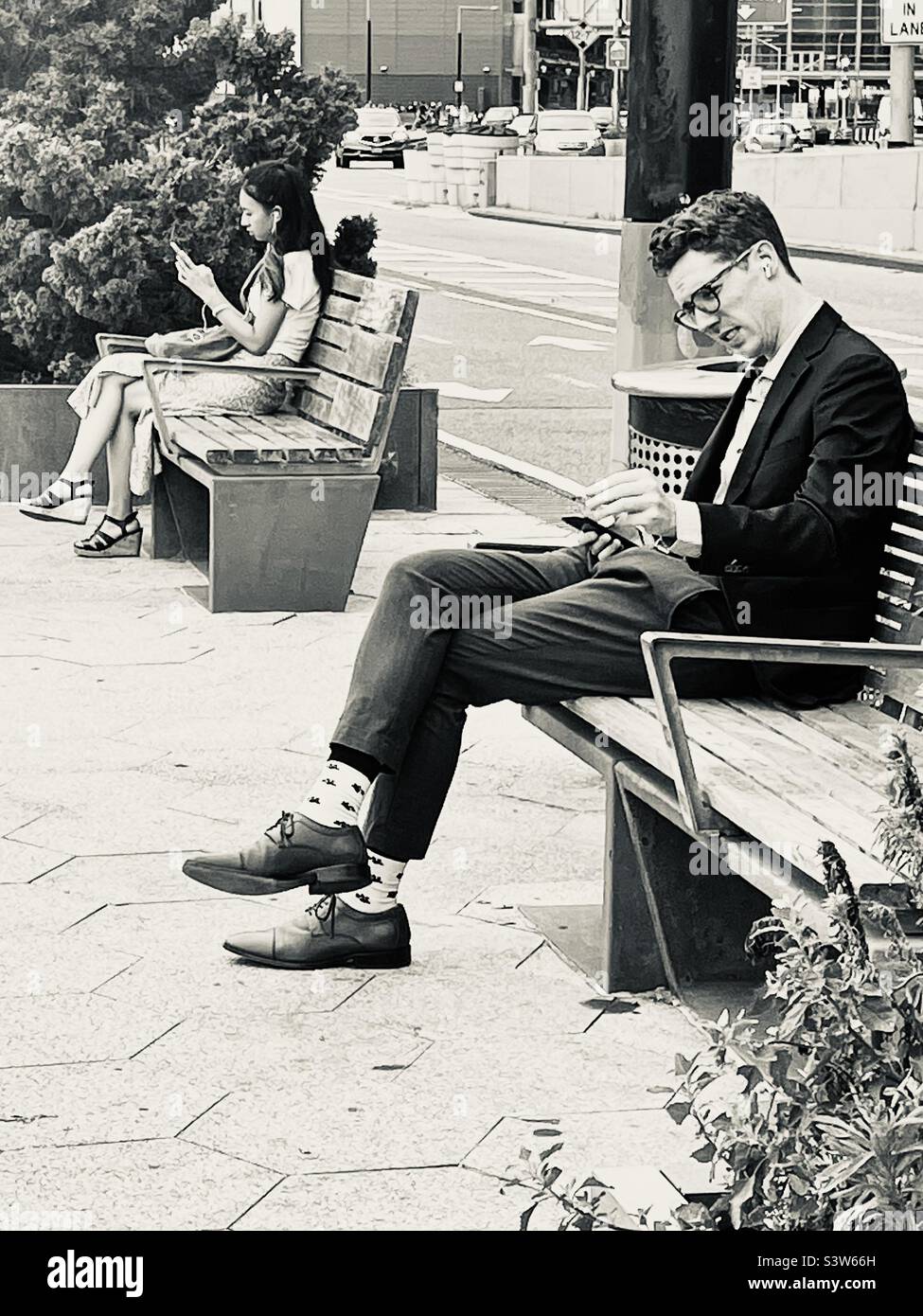 Black and white image of people looking at their cell phones while sitting on a city bench in New York City - Smartphone Captured Stock Image