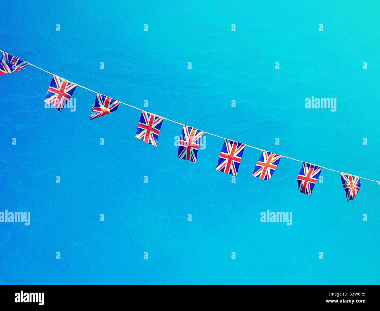Union Jack bunting flying in a sunny British sky. This is the collective flag of the United Kingdom. Photo ©️ COLIN HOSKINS. Stock Photo