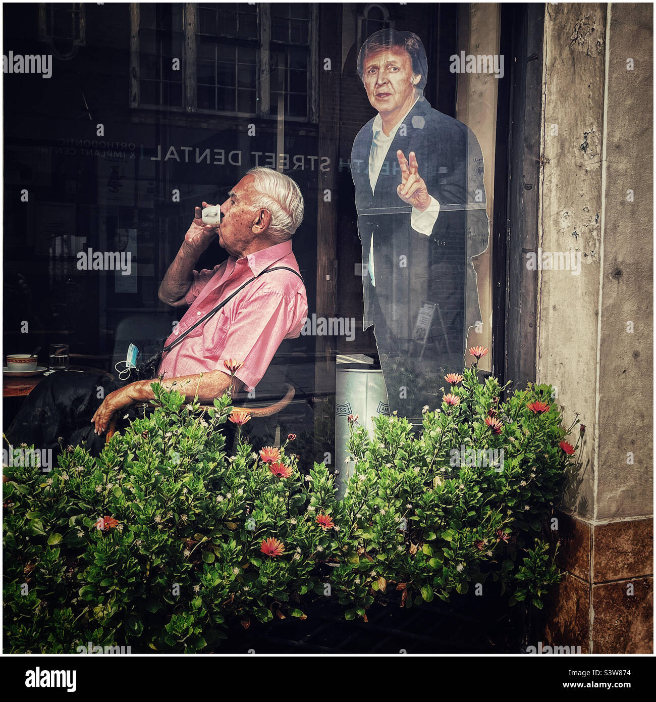 Man drinks coffee next to a life size cutout of Paul McCartney - Smartphone Captured Stock Image