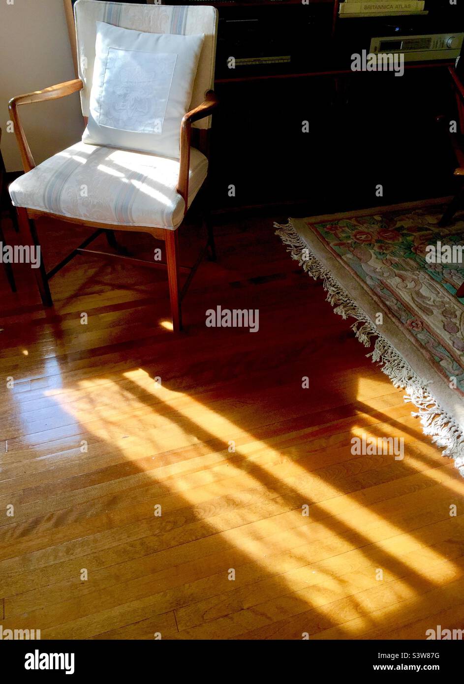 An empty chair and light streaming onto a gleaming hardwood floor. Stock Photo