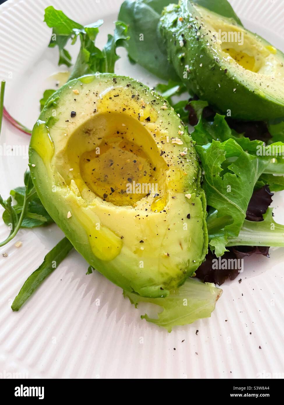 Close-up of a fresh avocado sliced on a bed of greens seasoned with kosher salt and cracked pepper Stock Photo